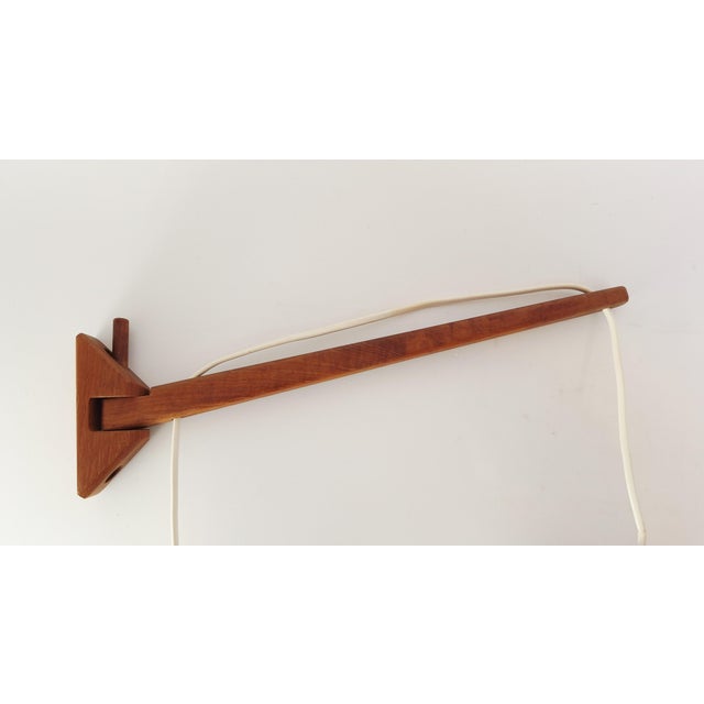 Swedish wall lamp from the 1950s–1960s with a solid teak wall mount and a swiveling arm. Fitted with a pleated silk or...