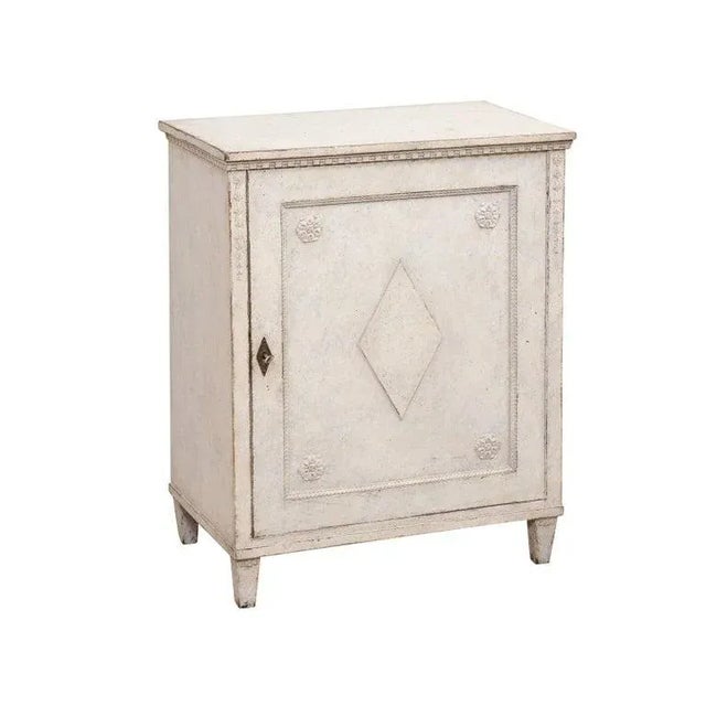 A Swedish Gustavian style painted wood cabinet from the late 19th century, with single door, carved rosettes, diamond...