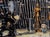 This oil painting depicts a whimsical scene featuring a ninja poised in action alongside a wooden mannequin and a small...