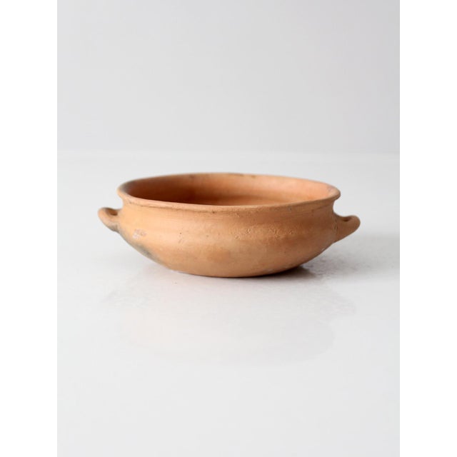 A charming antique terra cotta bowl with a low, rounded form, softly rolled rim, and two petite loop handles. Crafted from...