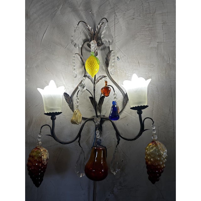 An elegant Venetian-style wall sconce, crafted from wrought iron and Murano blown glass. Its wrought iron frame forms...