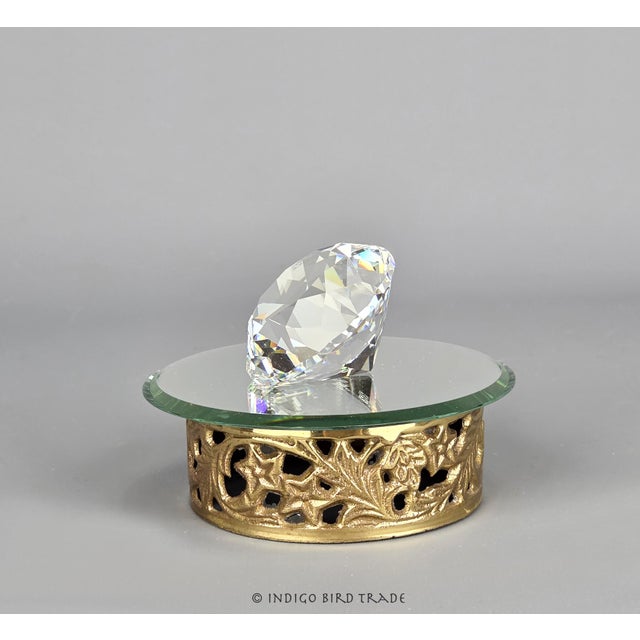 Singed Crystal Swarovski on the Mirrored Pedestal Display A clear, diamond-cut crystal sits on an ornate mirrored-top...