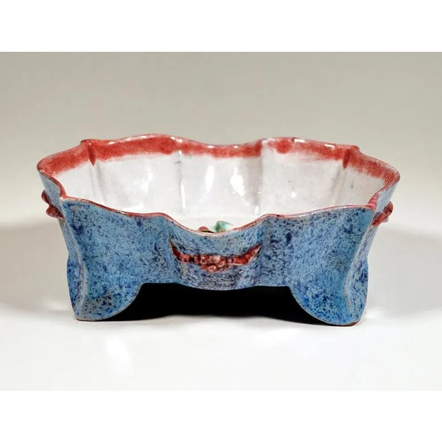 Bowl on an oval ground plan with flared, wavy and curved walls on four swept-out feet, fruit and leaf decoration in relief...