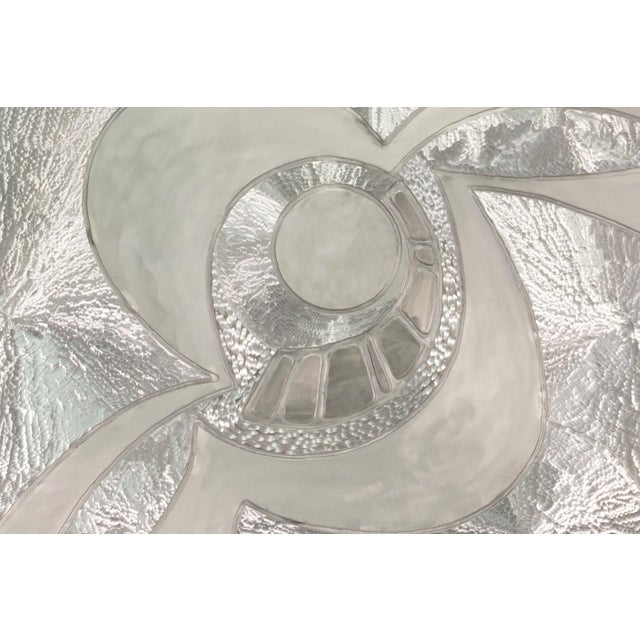A sculptural wall work by Greg Clark featuring an elegant swirling composition rendered in silver-toned metal. Defined by...