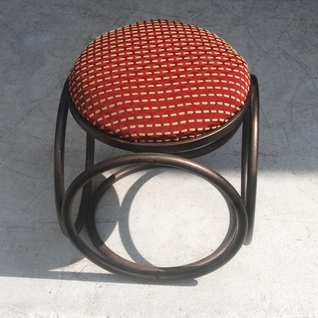 Thonet bentwood stool Has rounded, dark, bentwood base and a red fabric seat.