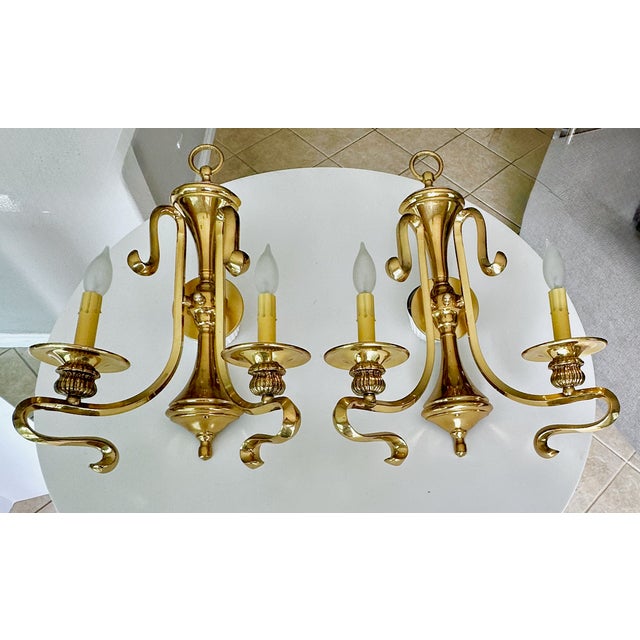 Pair of vintage French mid century polished brass two-light double-arm curved scroll wall sconces. Each uses 2 candelabra...