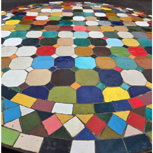 Beautiful round mosaic tile table featuring a vibrant multicolor tiled top and durable black wrought-iron style base. The...