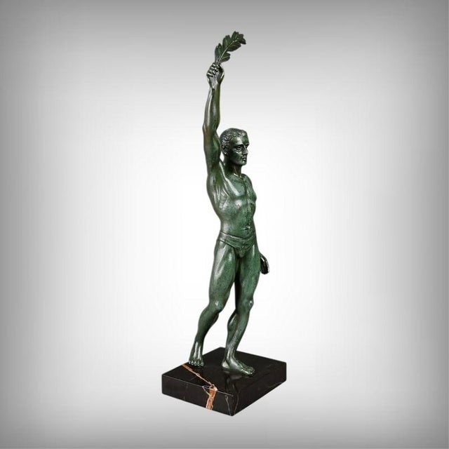 A superb Art Deco spelter sculpture with a green patina, depicting a male athlete in a victorious and elegant pose. The...