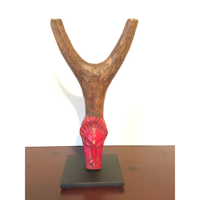 A colorful slingshot from the Baule people. Vibrant red handle is carved with opposing animal heads. Displayed on a custom...