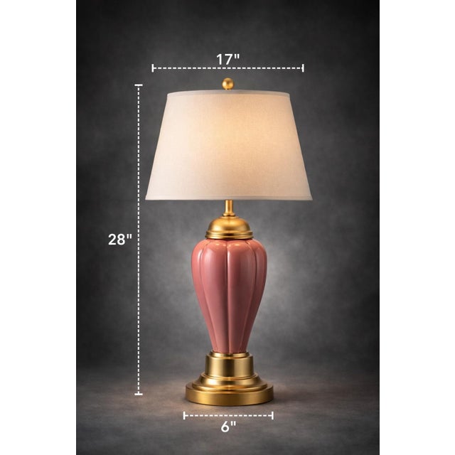 A classic Hollywood Regency table lamp featuring a fluted pink ceramic body paired with polished brass accents and a large...