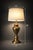 A classic antiqued brass urn table lamp with a large linen drum shade and elegant neoclassical silhouette. Warm brass...