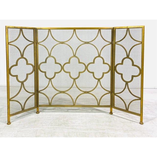 A well-crafted iron three-part fireplace spark screen in a gold finish with geometric patterns and a mesh screen to arrest...