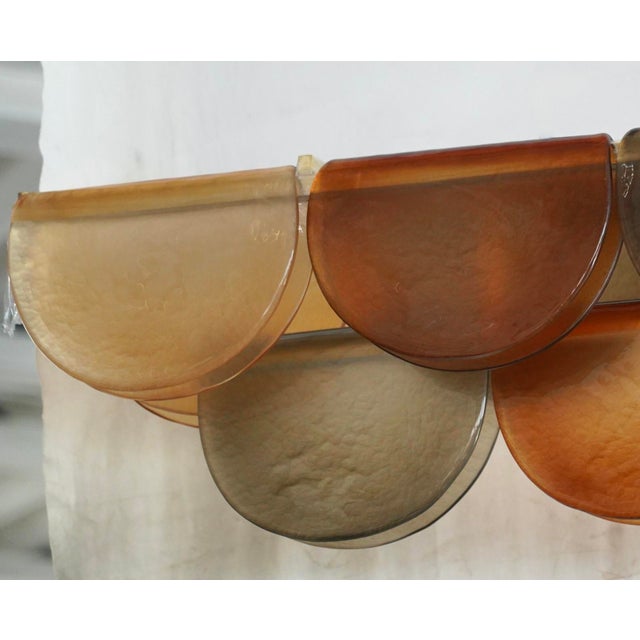 Murano chandelier with an elongated design, featuring a brass frame and unique glass in amber and smoky tones. All Murano...