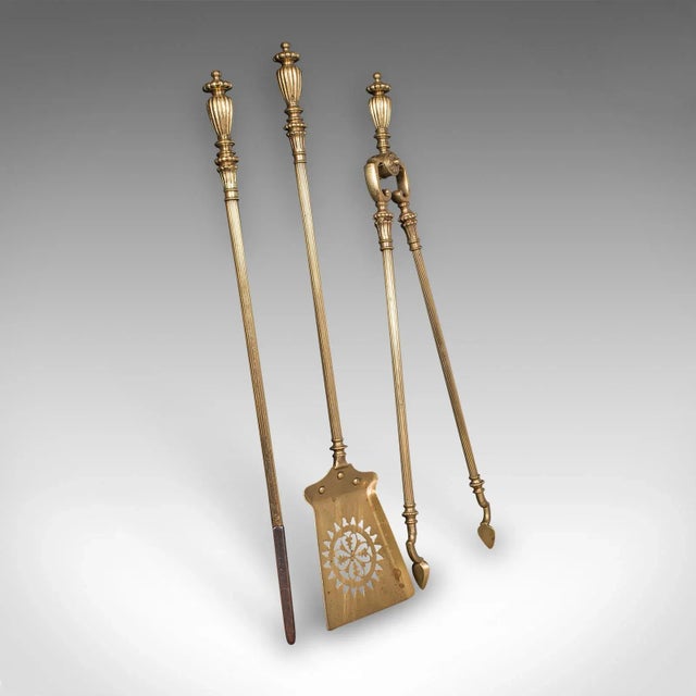 This is an antique fireplace tool suite. An English, brass shovel, poker and tong set with accompanying tool rests, dating...