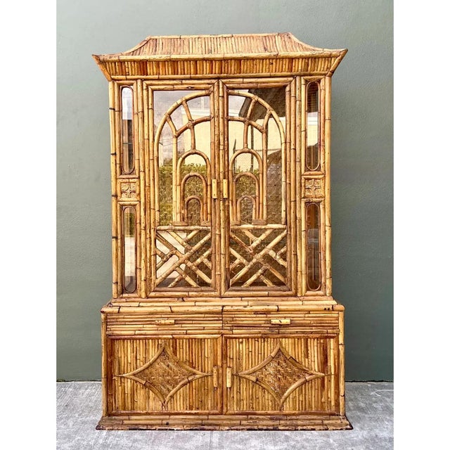 This vintage china cabinet is a tall, theatrical piece of chinoiserie craftsmanship, built from split and whole bamboo and...