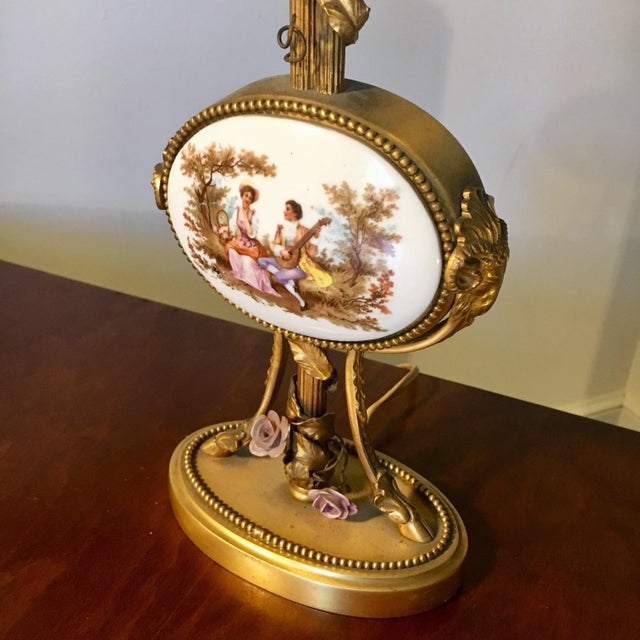 Lamp is primarily gold with two rams head and feet supporting an oval central plaque. Lemoges porcelain center is composed...