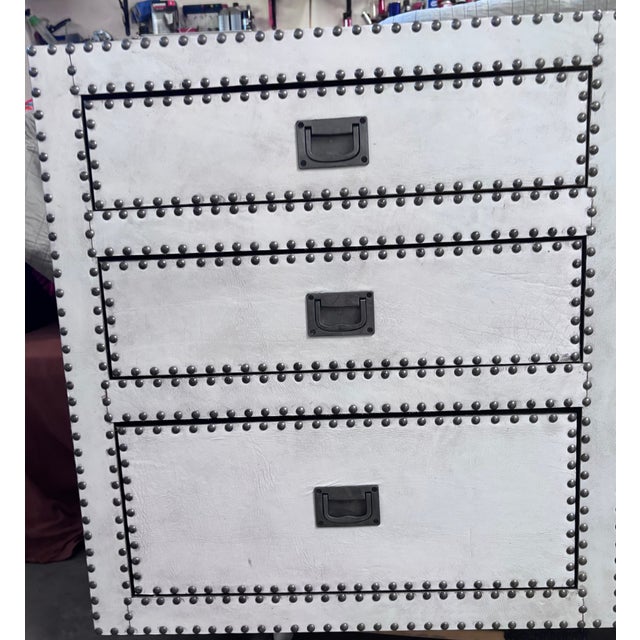 Wrapped in white leather with brass studs along edges and drawer fronts. Black interior of drawers