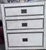 Wrapped in white leather with brass studs along edges and drawer fronts. Black interior of drawers