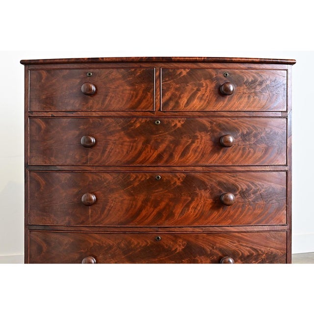 A classic English bowfront chest of drawers made of mahogany in the Regency style, circa 1870. The top surface is a large...
