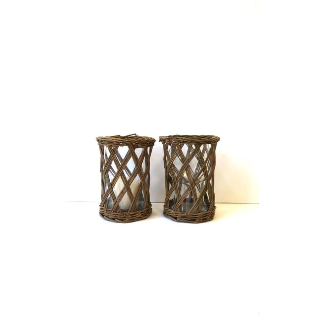 A set of two (2) wicker twig hurricane candle lamps. Set of wicker twig holders have a lattice 'X' design and glass...