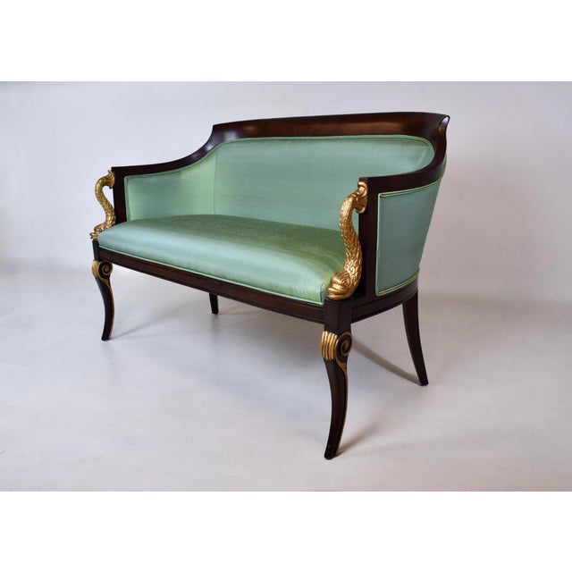 A classic French Empire Style curved back settee with distinct Neoclassical design elements in the carved gold dolphin...