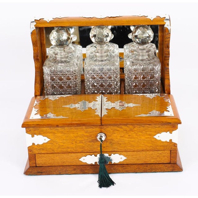 This is a superb antique Victorian golden oak cased three-decanter Tantalus with decorative silver-plated cut brass Gothic...