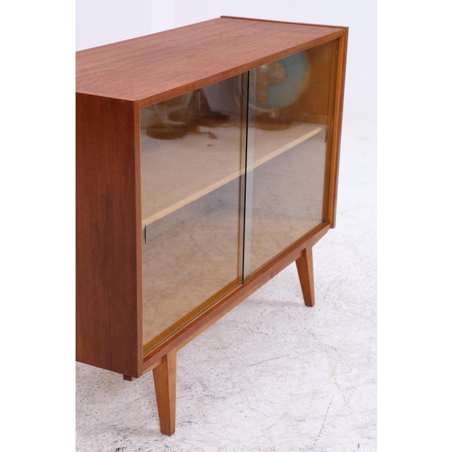 Vintage chest of drawers with delicate glass sliding doors and a slim base. The combination of open storage space and a...