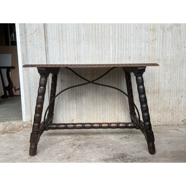 About 19th Spanish Side Table with cared turned legs and wood stretcher and also an iron stretcher The top has a carved...