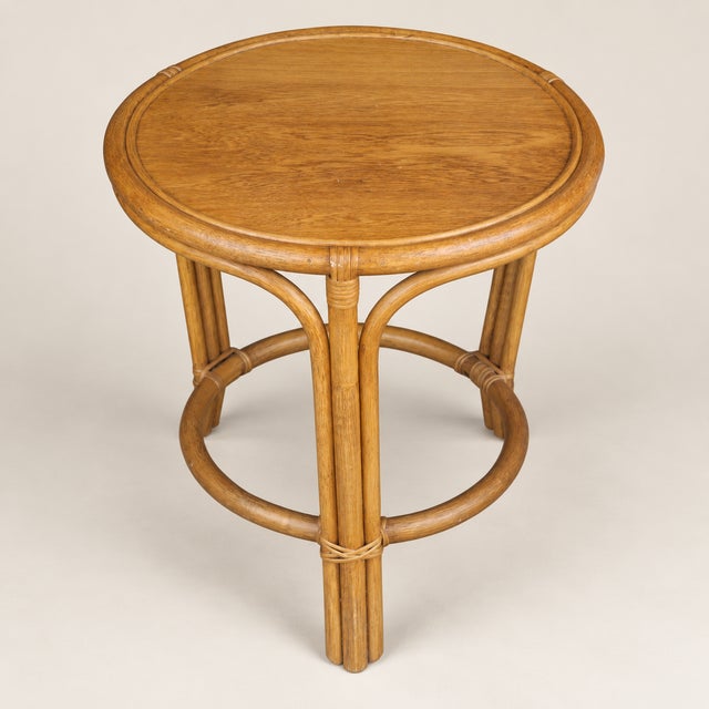 Late 20th century round occasional table in warm honey-toned bamboo and rattan with a fitted wood inset top. Three bundled...