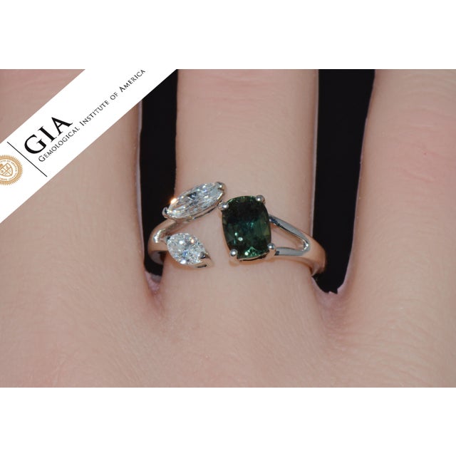 This exquisite designer ring features a GIA certified 1.52CT cushion modified brilliant cut bluish green sapphire set in...