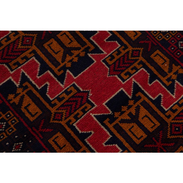 A beautiful Vintage Persian Balouch hand-knotted wool rug with a red field and multicolor accents in an all-over geometric...