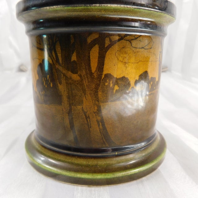 This is a brown and green Royal Daulton Tobacco Jar and matching lid. The jar has scenery on it of hills and land and...