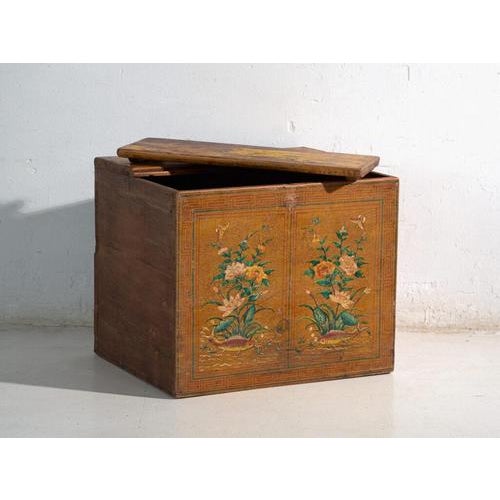 This antique painted trunk in pine wood features a front over an ochre yellow ground with two symmetrical panels showing...