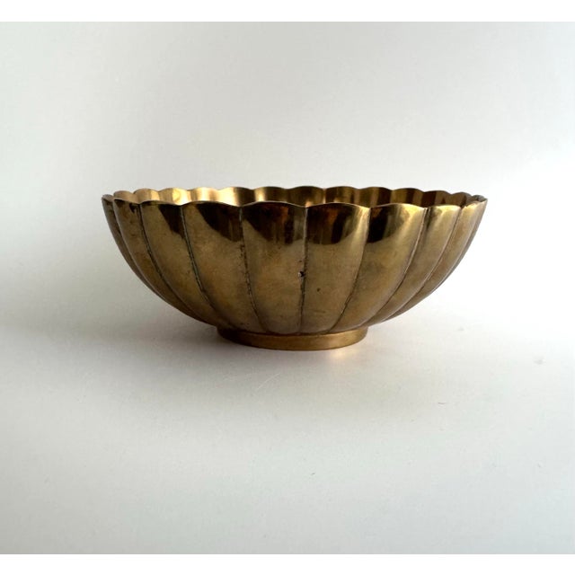Elegant vintage brass bowl featuring a beautifully fluted, scalloped design with a warm golden patina. Its reflective...