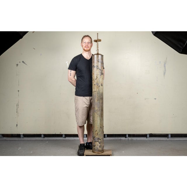 A tall cylindrical floor lamp repurposed from an industrial wooden wallpaper and textile printer in muted silver-grey and...