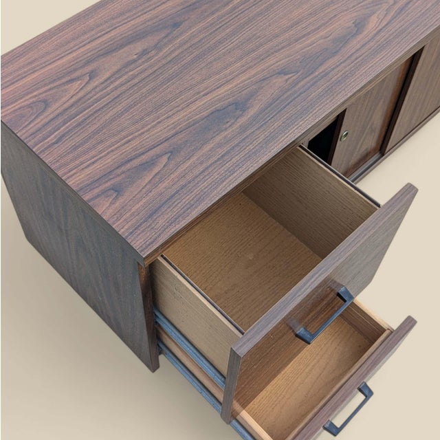 A long, low 1970s credenza with a warm walnut-grain laminate finish, clean architectural lines, and generous concealed...