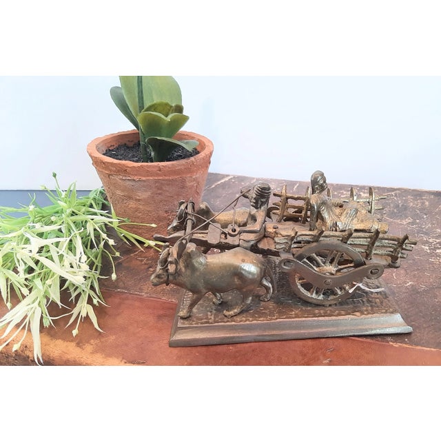 This vintage brass sculpture, handcrafted in India, features a driver with a cart and oxen, along with a passenger riding...