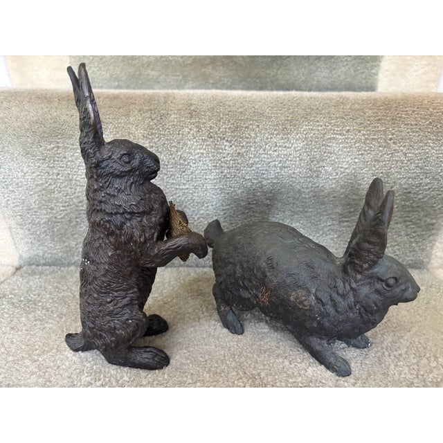 An unmatched pair of bronze rabbits, one standing on hind legs holding a little woven brass basket; the other, in a...