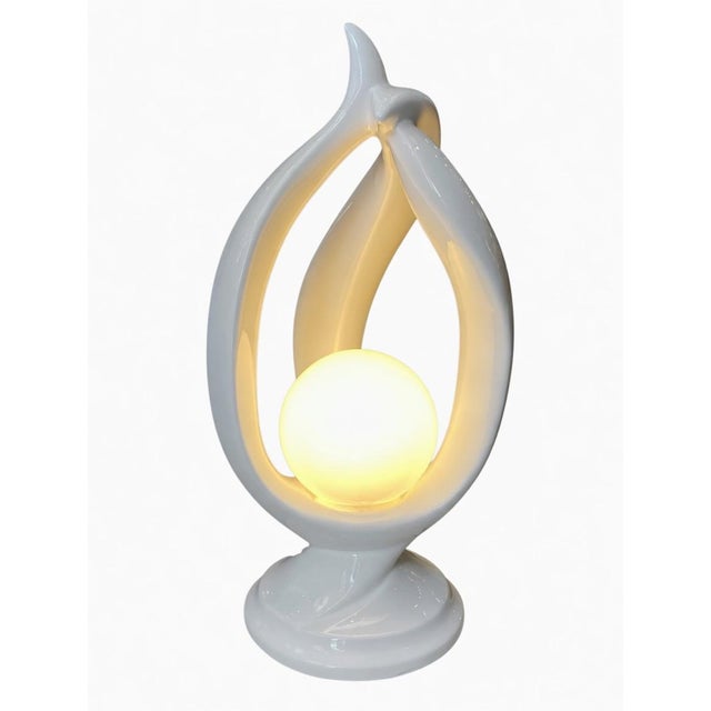 Modern white ceramic sculptural table lamp with abstract intertwined organic forms and glowing spherical orb. Elegant...