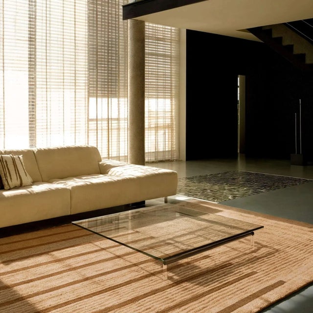 The TanLines Rug blends beige and nude tones with soft brown striped details, evoking sun-warmed sand and shadows. The...