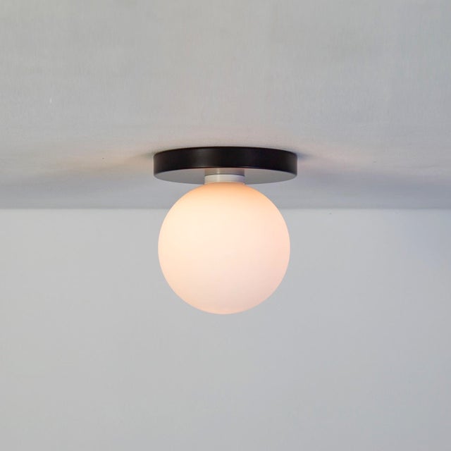 Minimal from top to bottom. This black flush mount pairs a metal base with a soft glass globe. Cool, calm, and quietly...