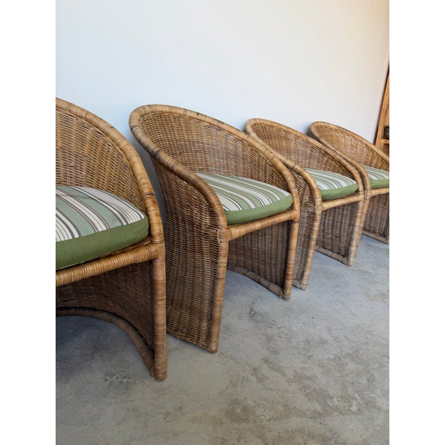 A beautiful set of four 1970s vintage wicker dining chairs featuring a classic barrel back silhouette with an organic,...