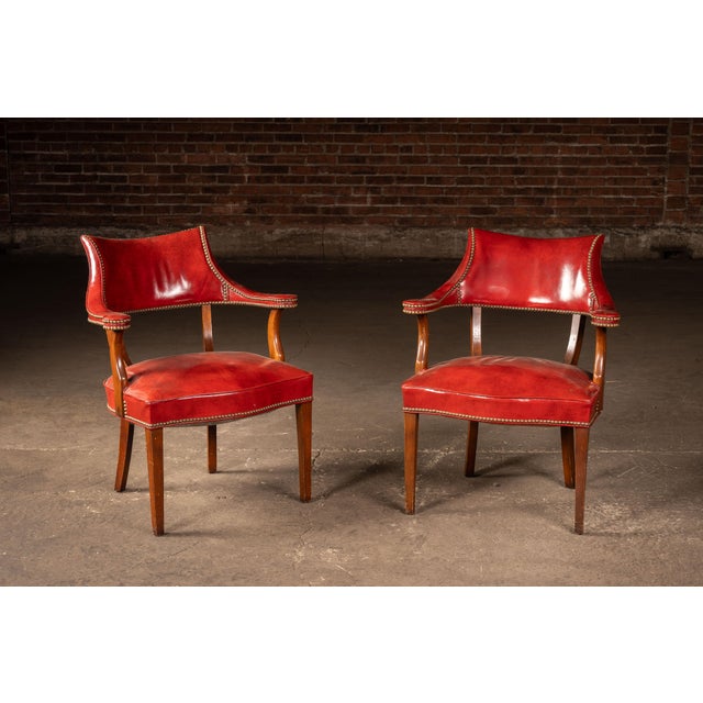 Matching pair of classic captain's armchairs upholstered in richly patinated burnt orange leather with brass nailhead trim...