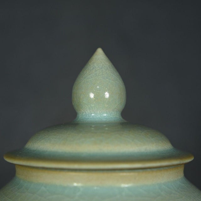 A round, softly curved porcelain jar with its lid, finished in a celadon-green glaze with a fine crackle (ice-crackle)...