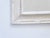 This carved wood, whitewashed mirror measures 30.5"H x 21.25"W.