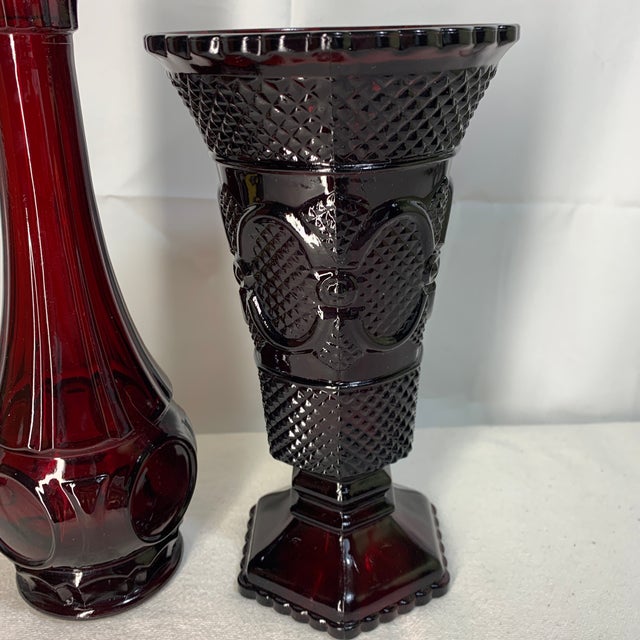 The items shown are vintage ruby red glass pieces from the Avon 1876 Cape Cod Collection, featuring a tall bud vase and an...