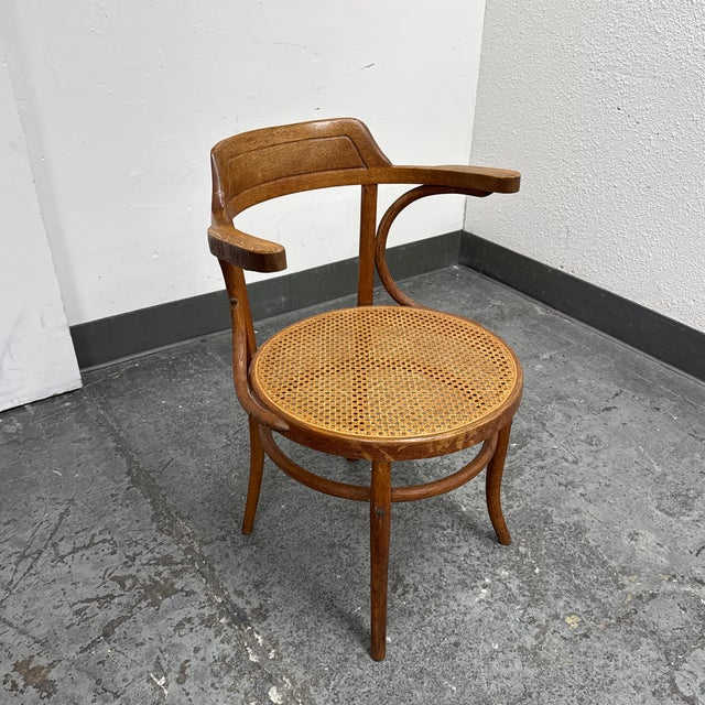 Design Plus Gallery presents a Vintage Bentwood Cane Seat Armchair from Thonet. This distinctive chair showcases a curved...