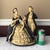 A beautifully sculpted and generously sized ceramic figurine depicting a Victorian-era couple in formal dress. The...