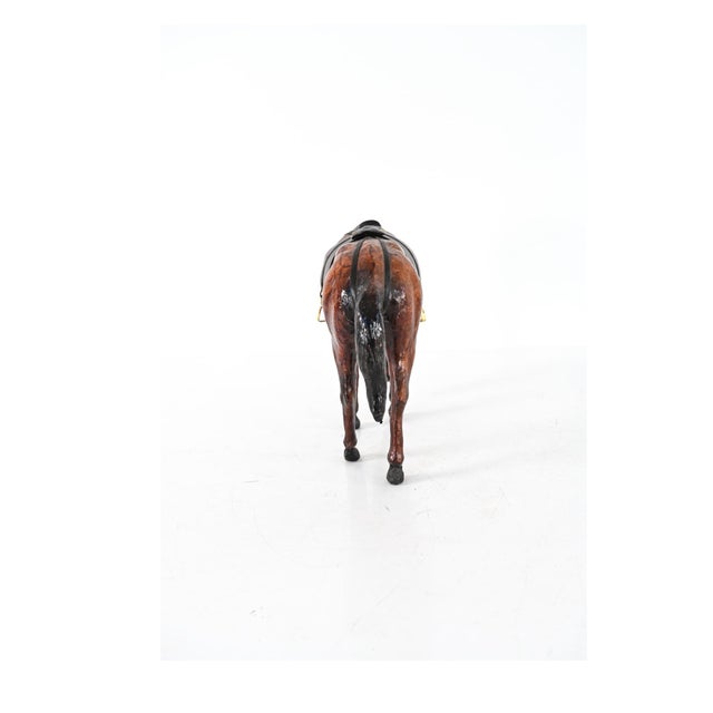 A leather-wrapped model horse sculpture in a glossy brown leather with its head lowered, black leather mane, tail, and...