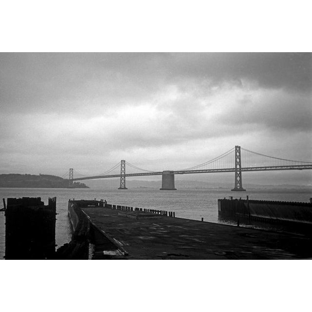 San Francisco, California, 1960s, black and white view of the Bay Bridge on a cloudy day. The photograph captures the...